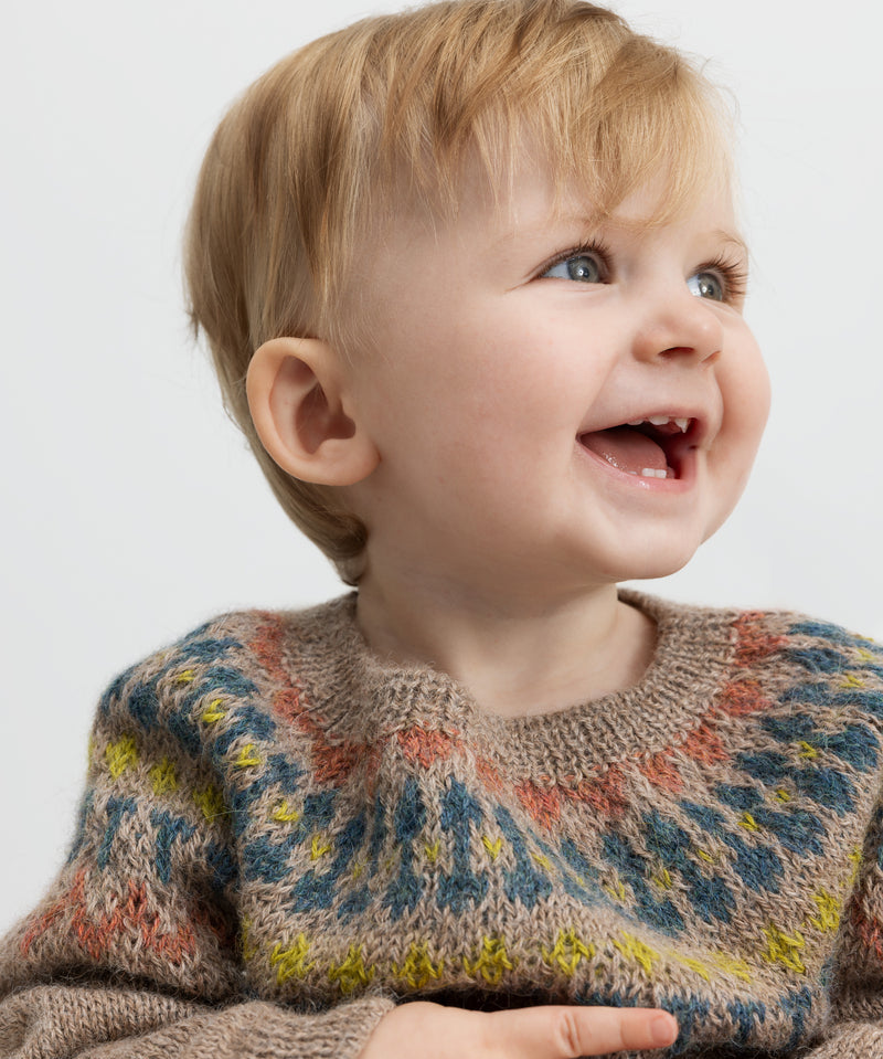 Smilende baby iført strikket trøje med farverigt mønster.