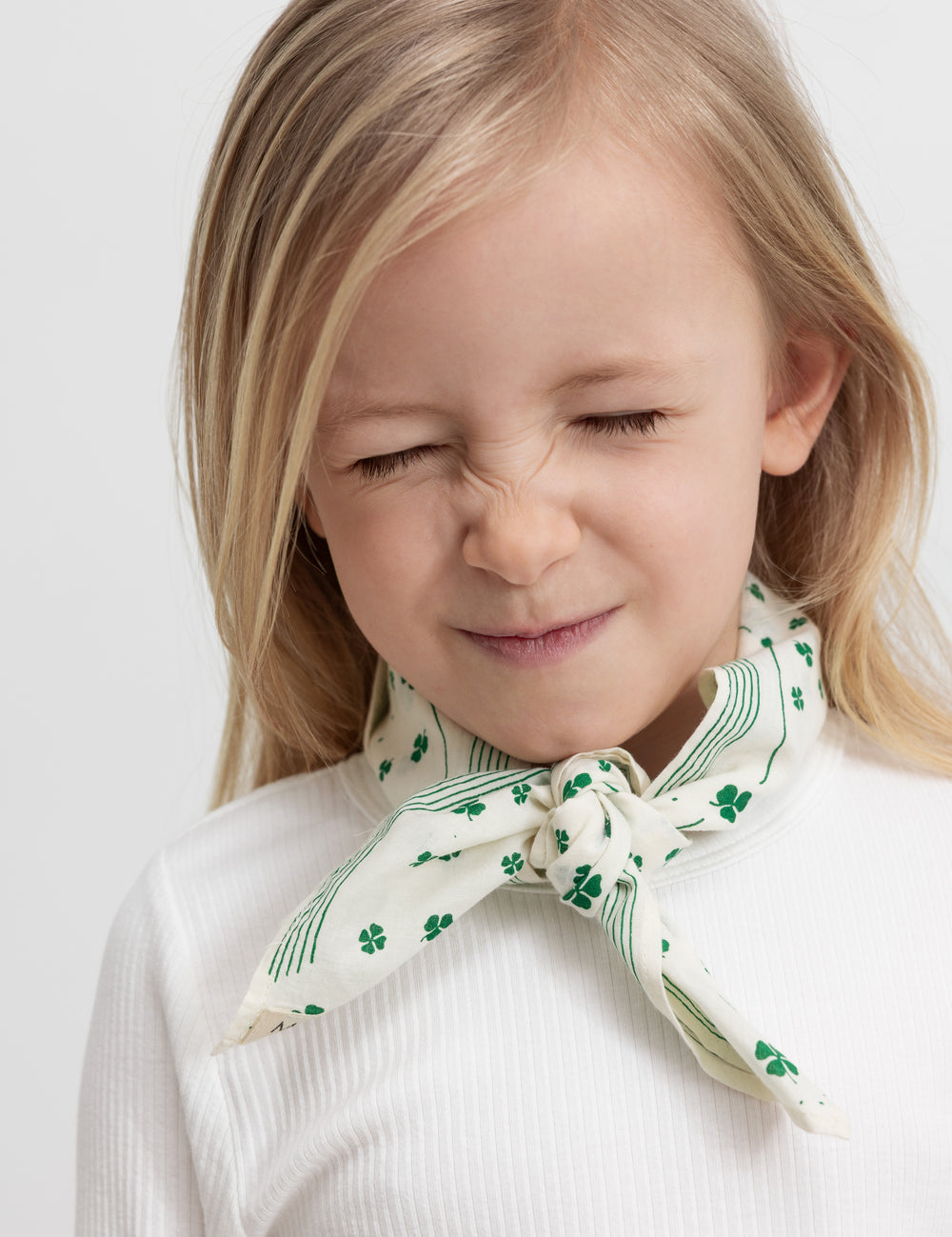 Wearing a beige handkerchief with a green clover print tied around the neck.