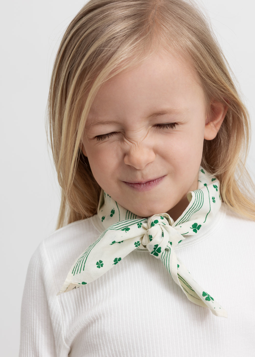 Wearing a beige handkerchief with a green clover print tied around the neck.