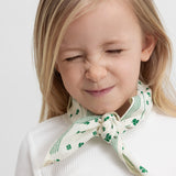 Wearing a beige handkerchief with a green clover print tied around the neck.