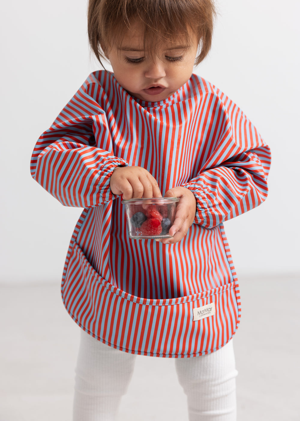 Stribet apron with long sleeves in blue and red, front pocket.