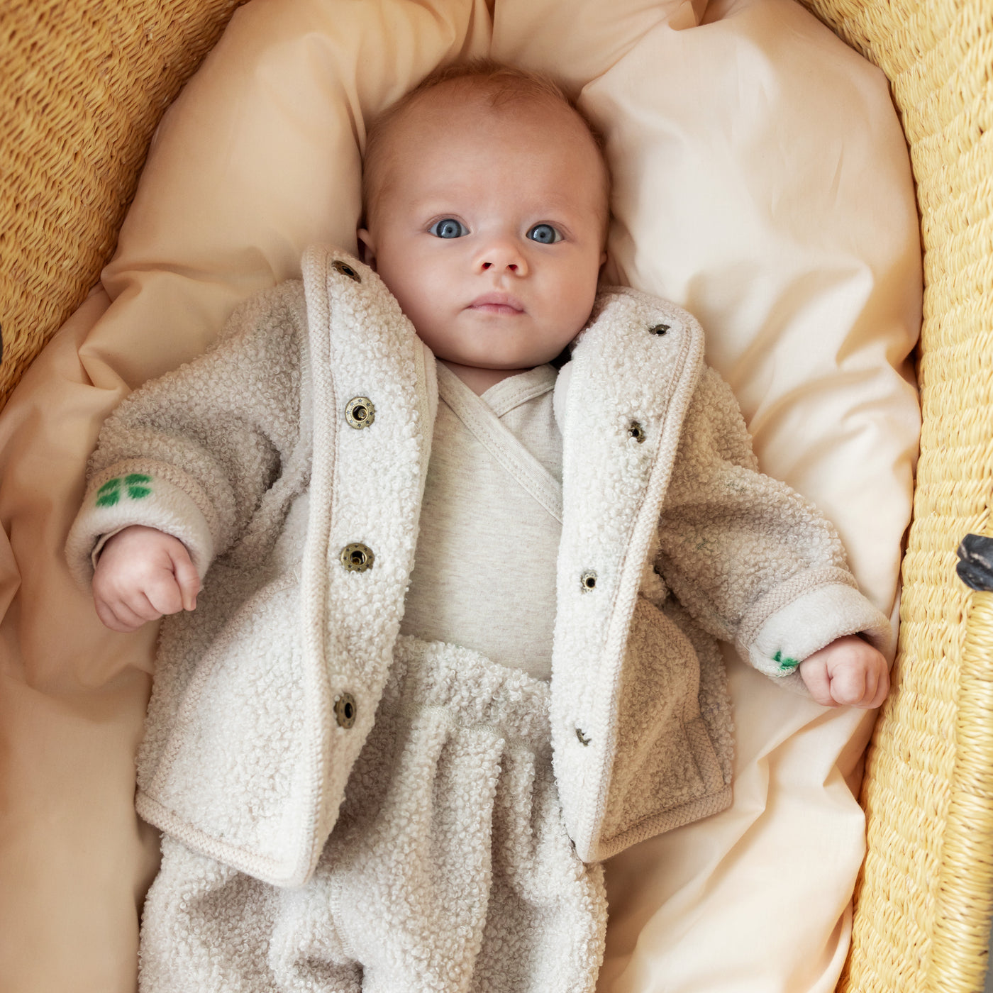 Baby iført beige teddyjakke og matchende bukser liggende i babynest