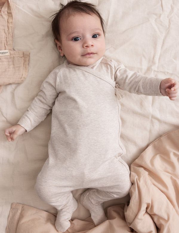 Nyfødt baby i beige heldragt liggende på sengetøj