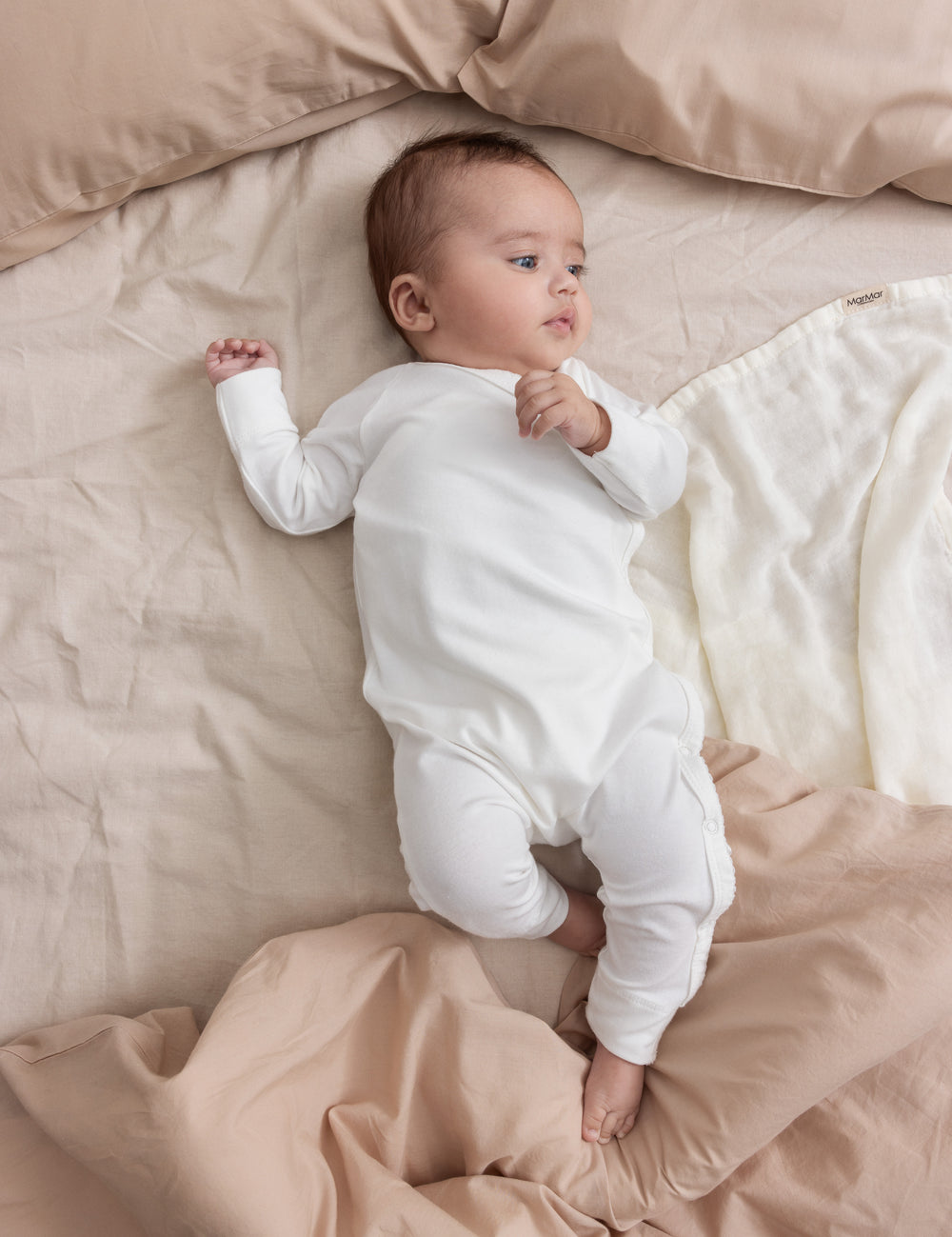 Baby wearing beige/grey knitted set lying in wicker basket with beige blanket.