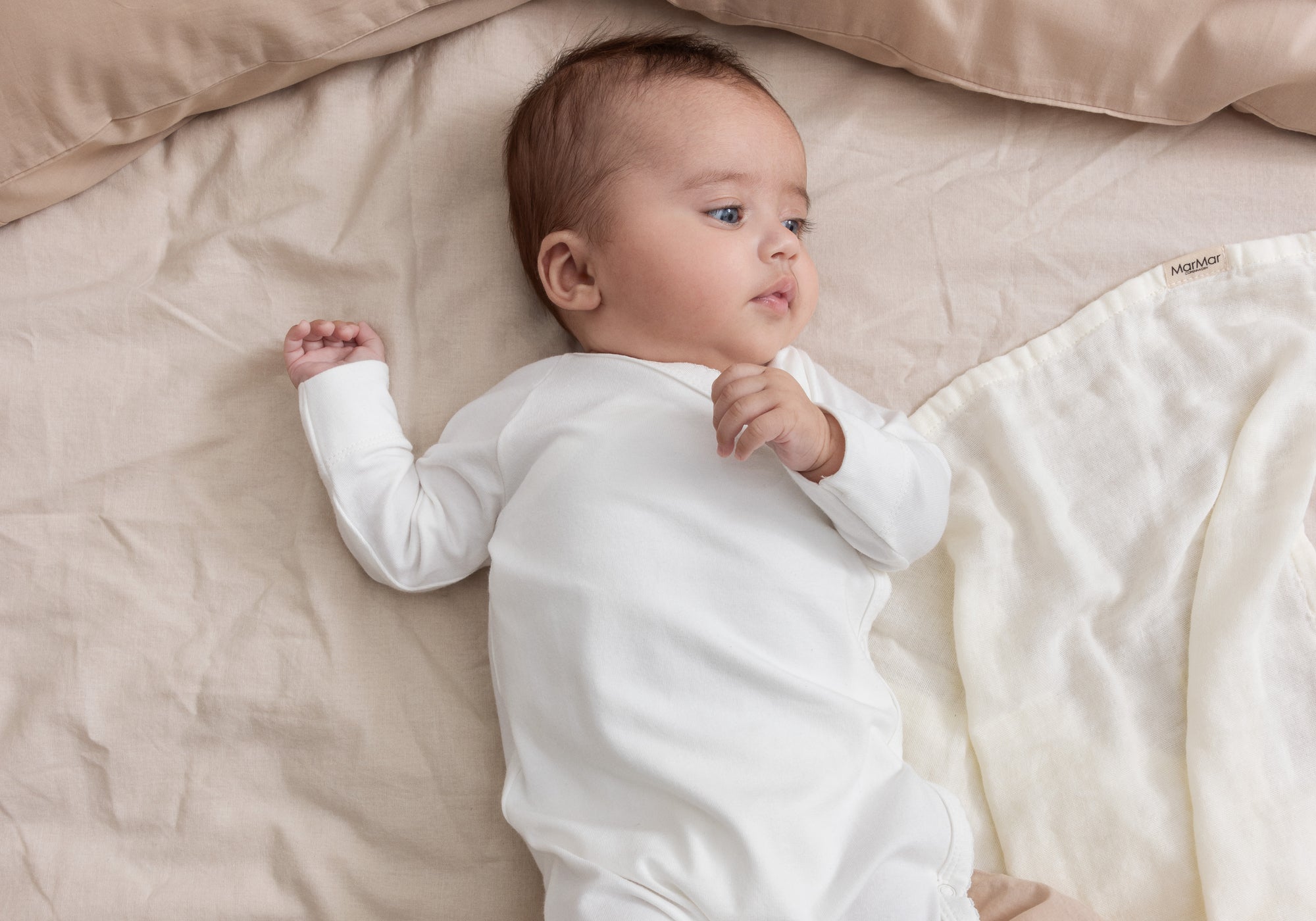 Nyfødt baby i hvid body liggende på beige sengetøj