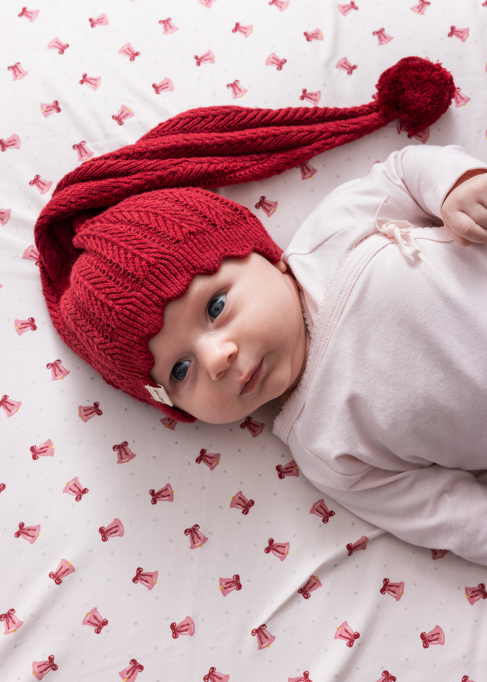 Baby iført rød strikket nissehue med kvast og lyserødt juletøj