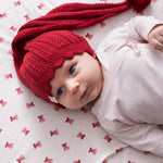 Baby liggende på cremefarvet tæppe med røde juleklokker