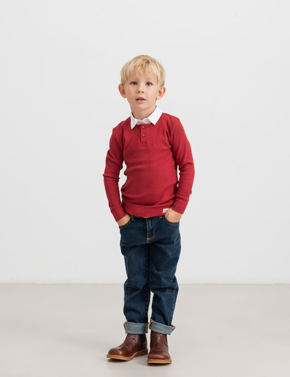 Dreng iført rød ribbluse, hvid skjorte og mørke børnejeans.