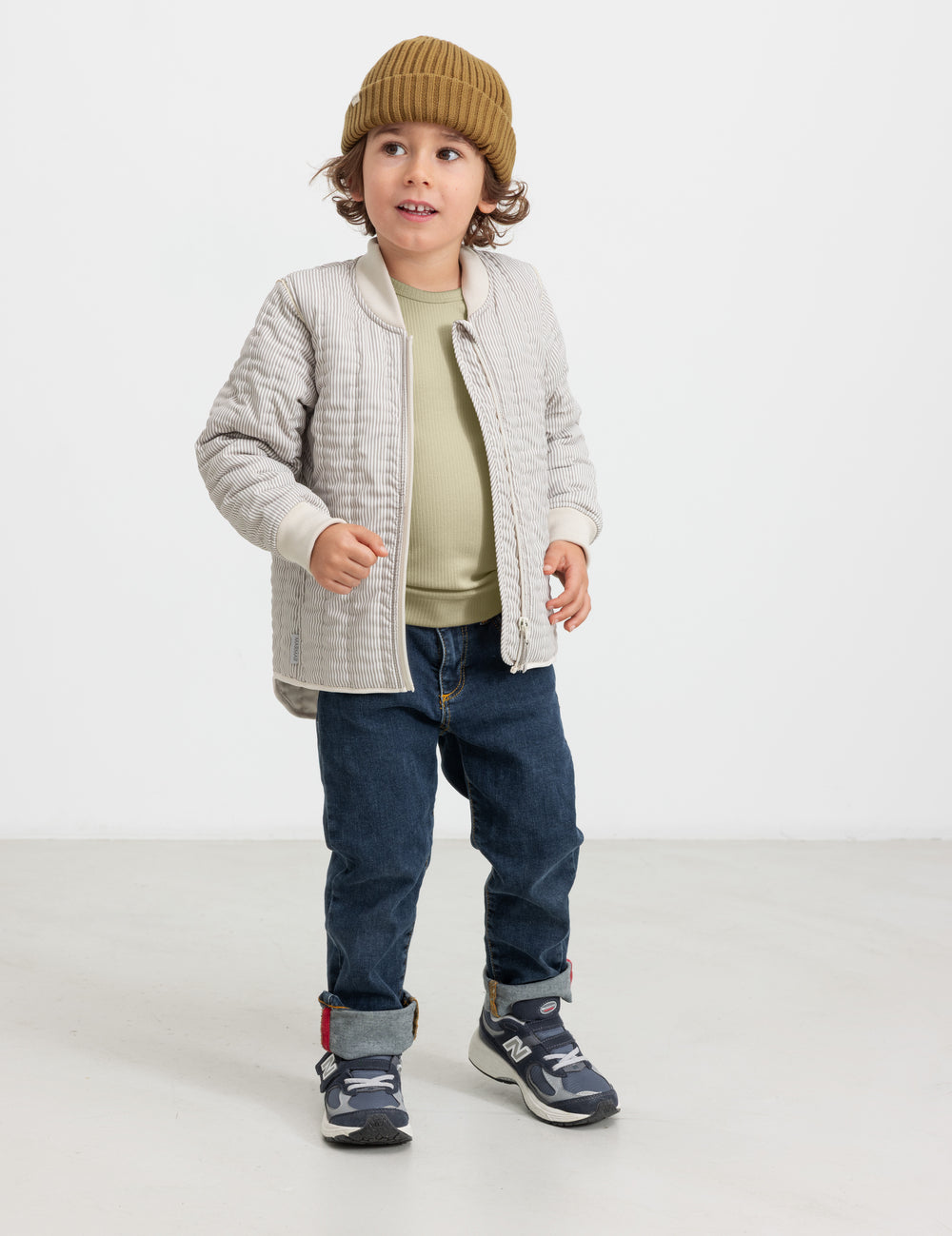 Child wearing a brown knitted hat with jeans and a jacket.