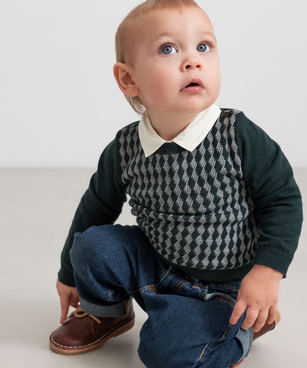 Baby iført mørkegrøn ternet strikbluse med skjortekrave og jeans