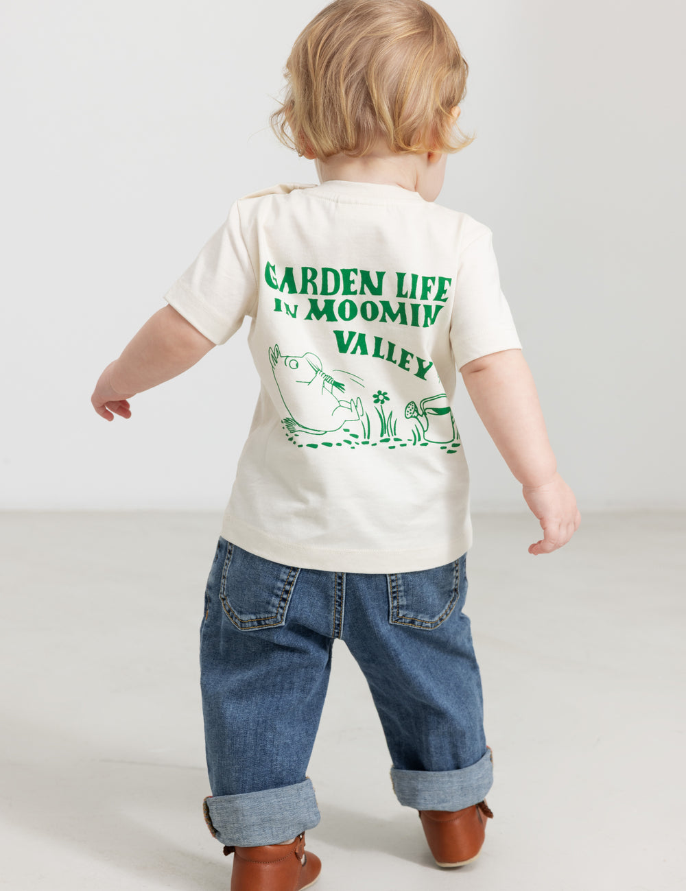 Baby wearing a white T-shirt with a green Moomin print and jeans.