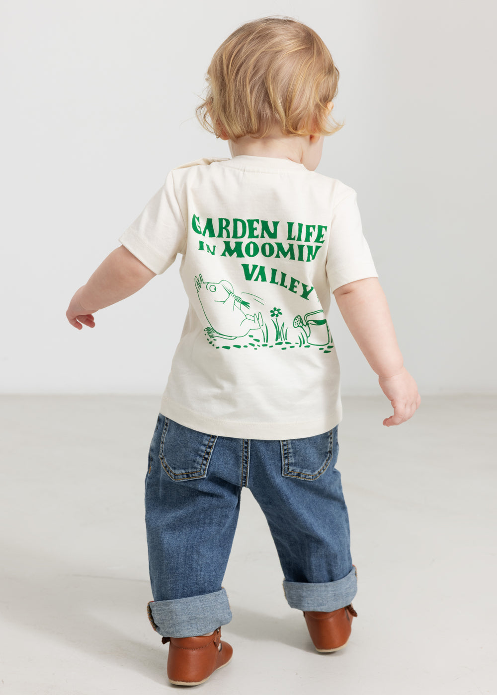 Baby wearing a white T-shirt with a green Moomin print and jeans.