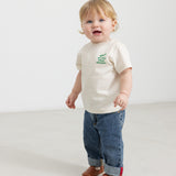 Baby wearing a white T-shirt with a green Moomin print and jeans.