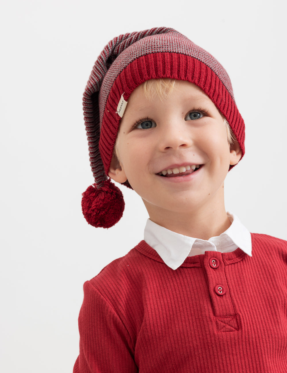 Boy wearing knitted Santa hat with red and gray stripes and red sweater for children