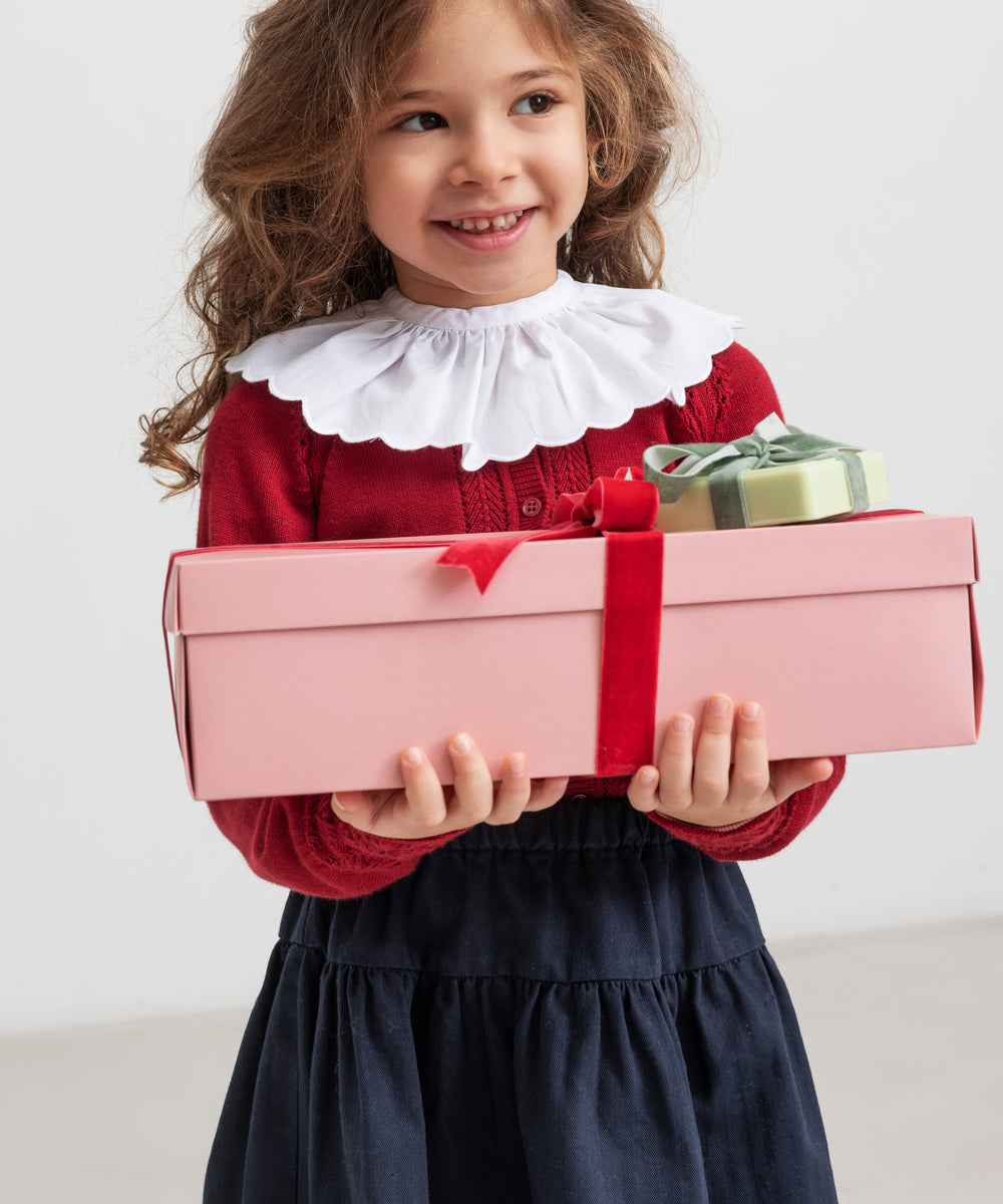 Pige holder julegaver iført mørkeblåt nederdel og rød bluse med hvid krave,