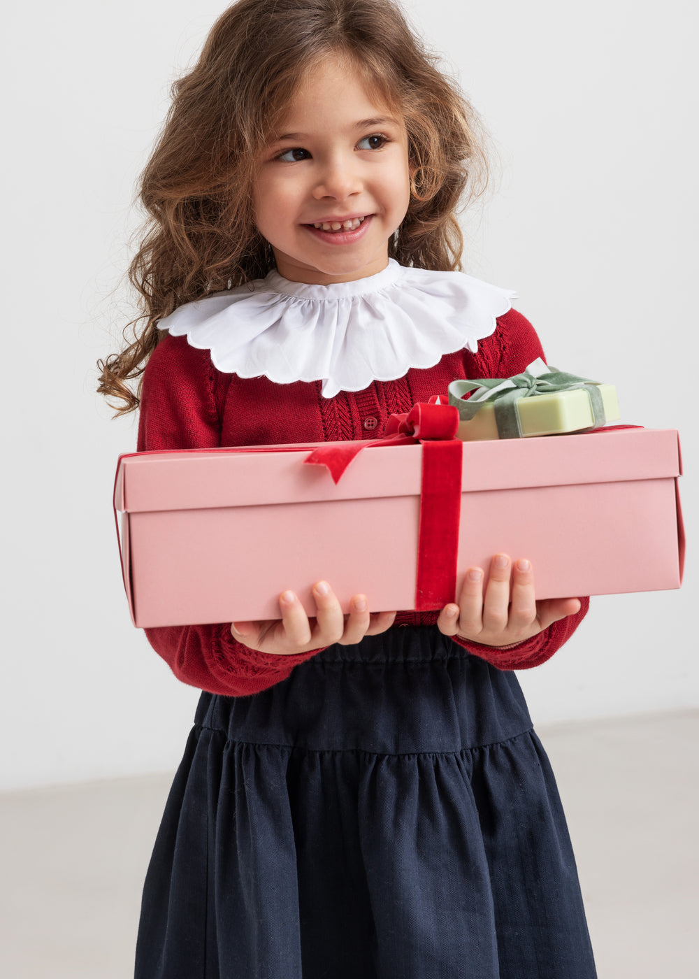 Pige holder julegaver iført mørkeblåt nederdel og rød bluse med hvid krave,