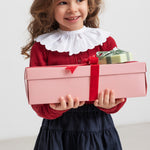 Pige holder julegaver iført mørkeblåt nederdel og rød bluse med hvid krave,