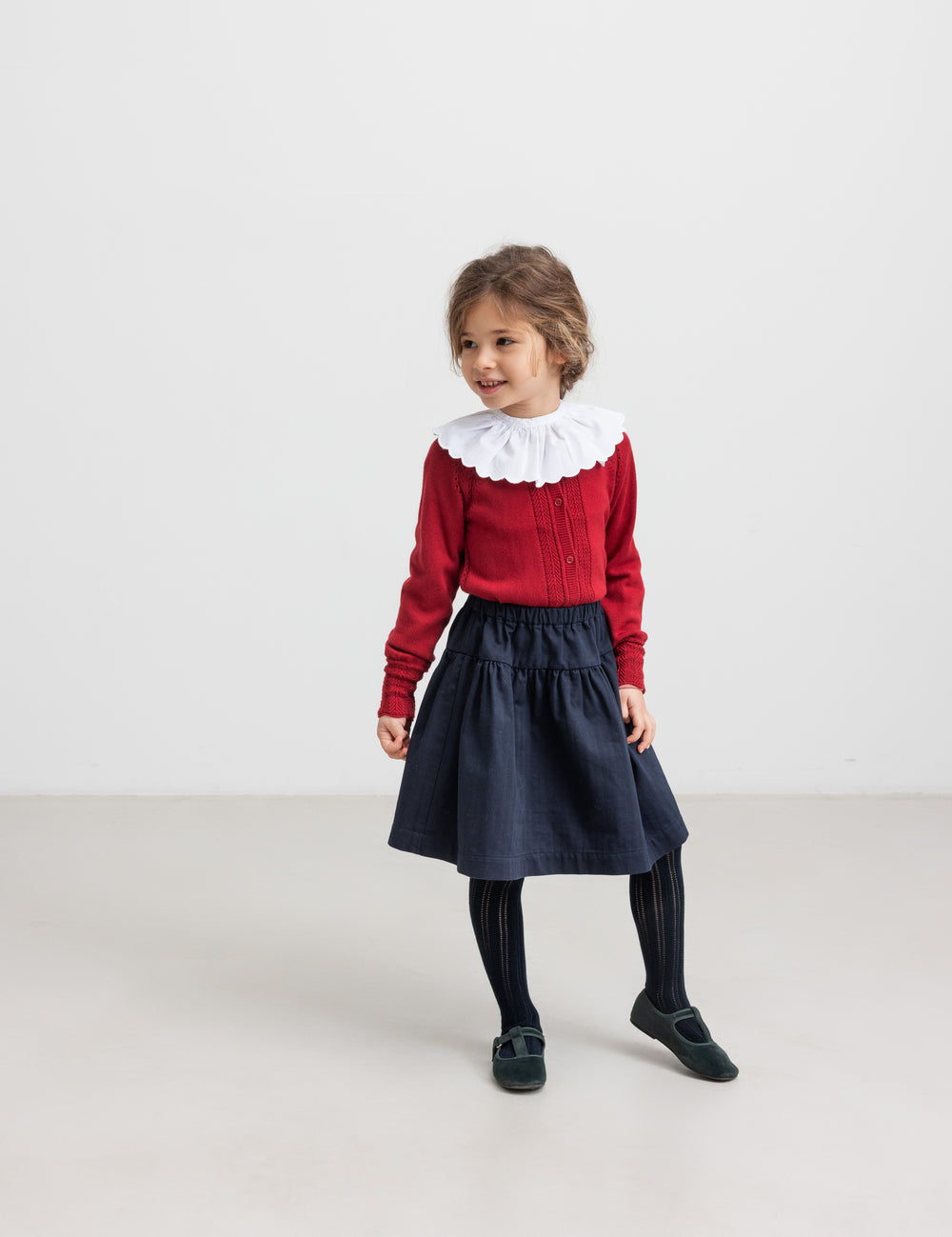 Girl wearing red Christmas sweater with lace pattern, white collared blouse and dark blue party skirt for children