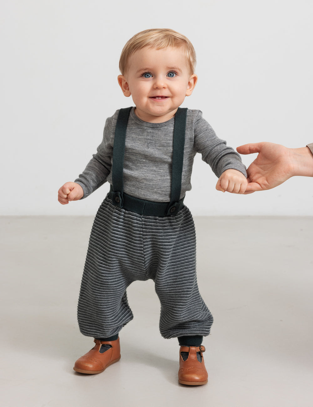 Baby iført mørkegrønne strikkede bukser med seler og grå bluse