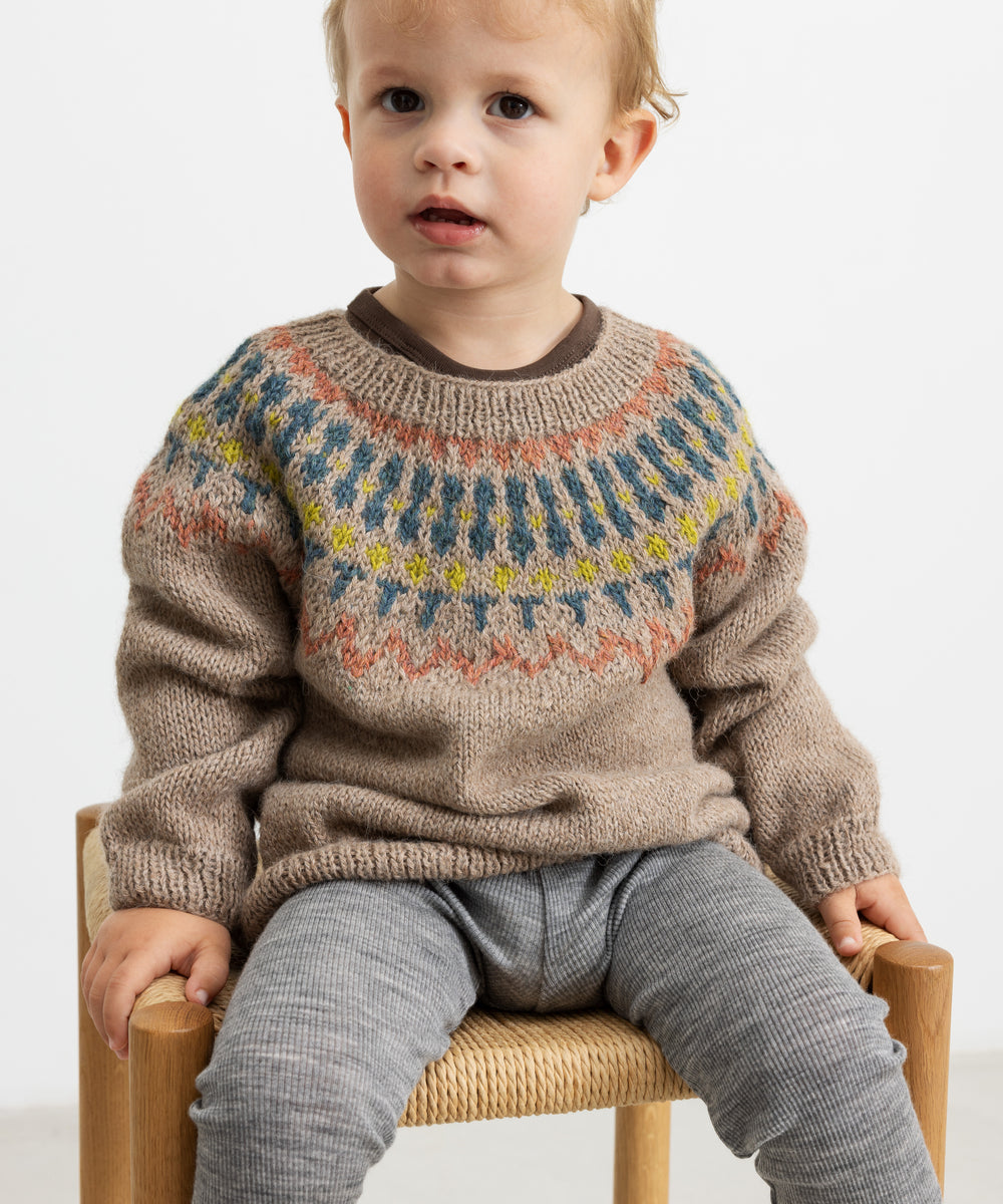 Dreng iført beige uldstrikbluse med mønster sidder på stol