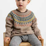 Dreng iført beige uldstrikbluse med mønster sidder på stol