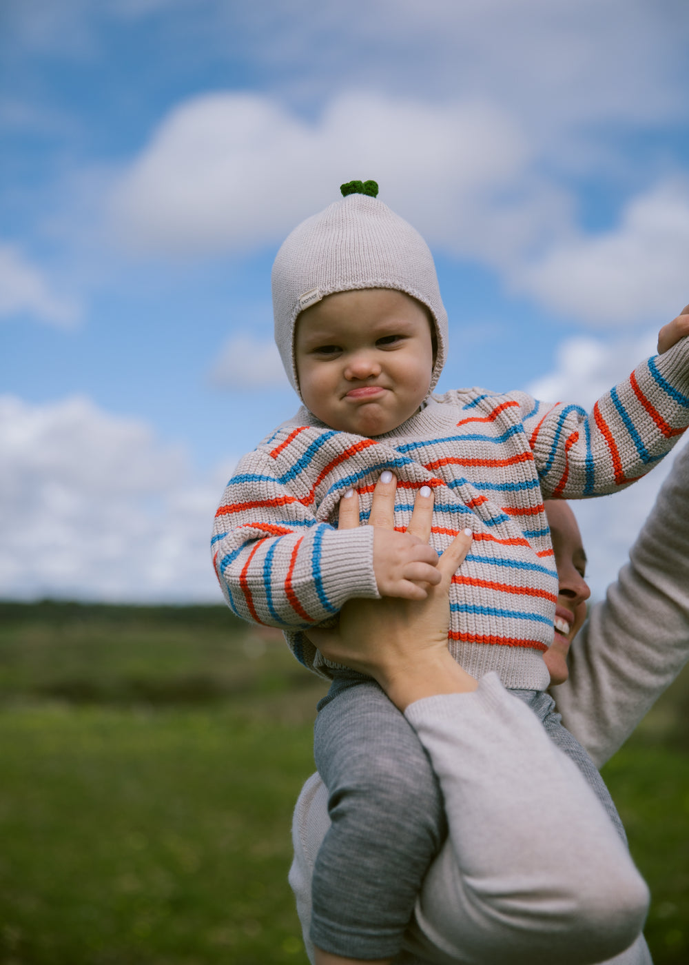 Baby is wearing a striped sweater and hat outdoors.