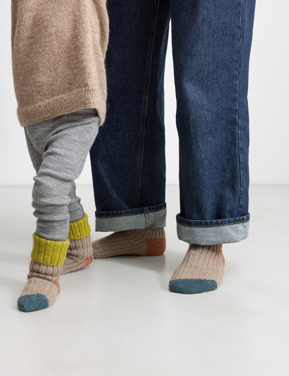 Barn iført uldstrømper i beige med grøn rib, orange hæl og blå tå