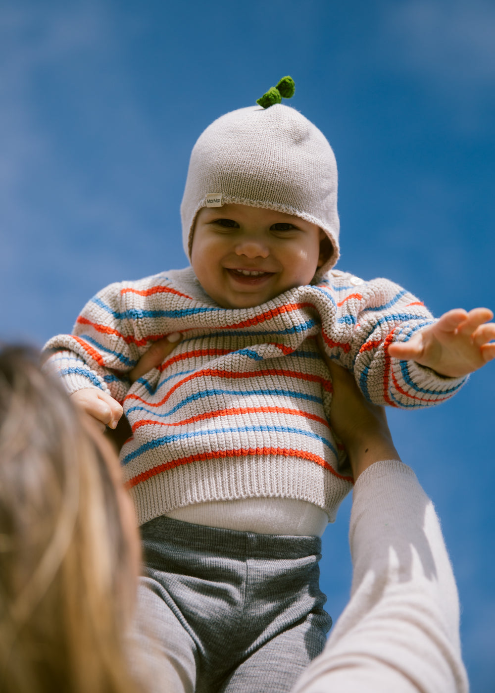 Baby is wearing a striped sweater and hat outdoors.
