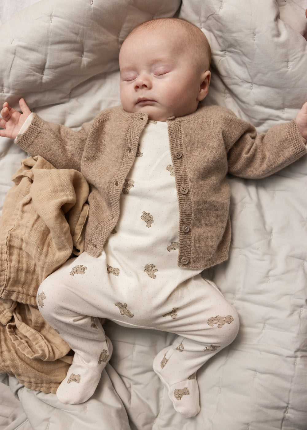 Baby onesie in white with beige teddy bear print, visible with long legs.