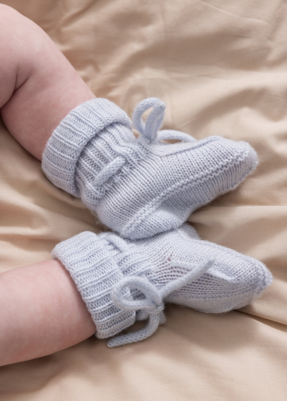 Light blue knitted baby shoes on a model with tied laces.