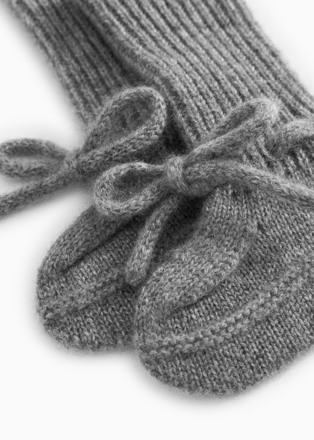 Close-up of a gray knitted baby bootie with a ruffle detail over the ribbed edge.