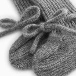 Close-up of a gray knitted baby bootie with a ruffle detail over the ribbed edge.