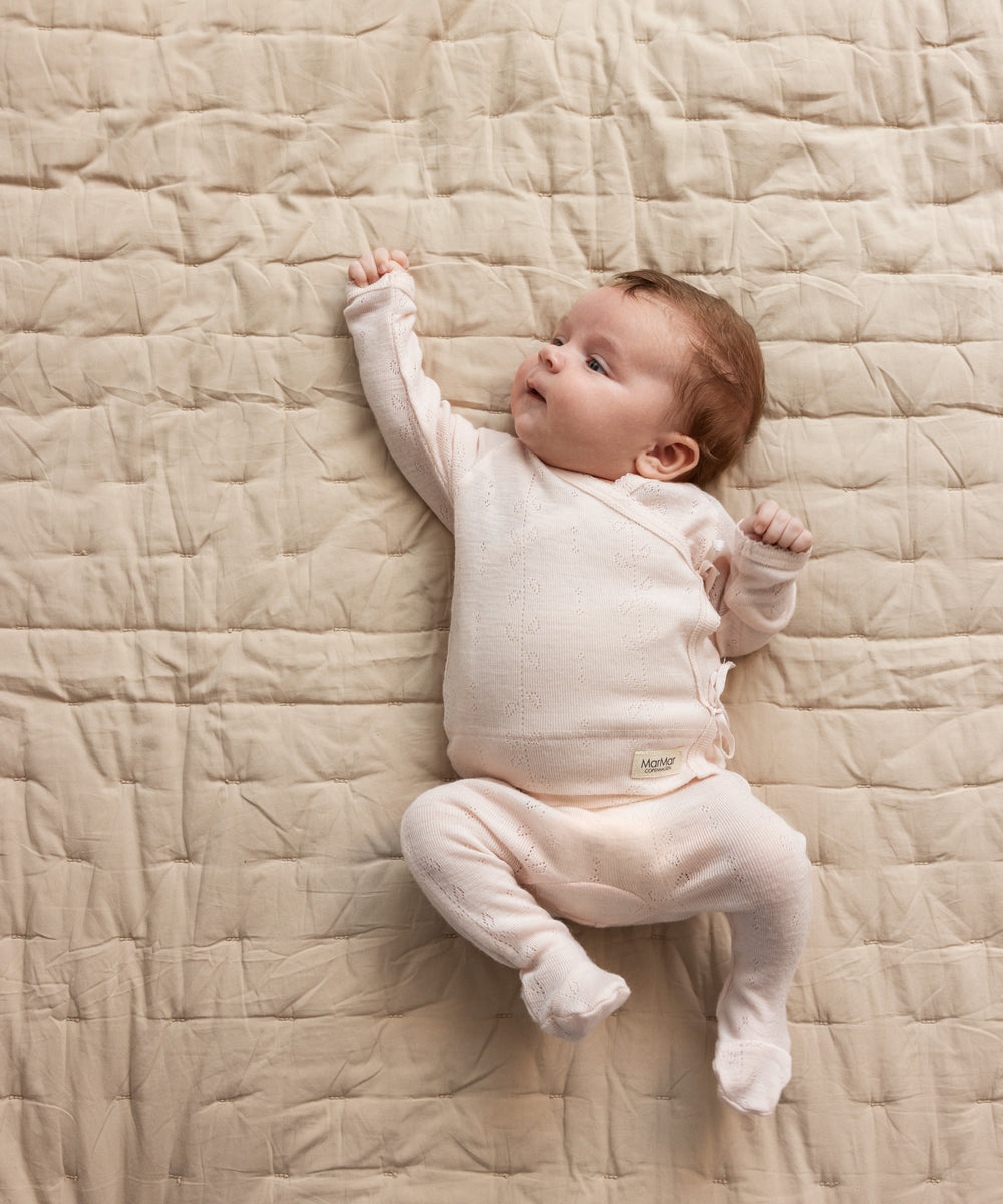 Baby iført lyserød heldragt i merinould ligger på tæppe