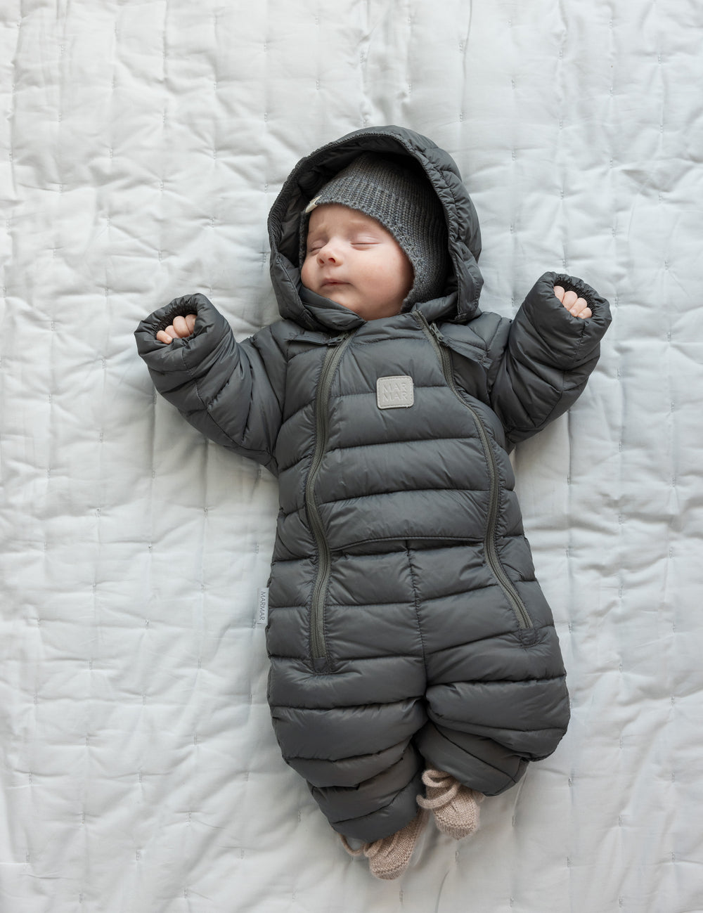 Baby ligger på tæppe iført mørkegrå dundragt.