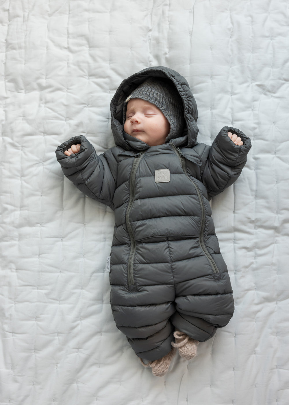 Baby ligger på tæppe iført mørkegrå dundragt
