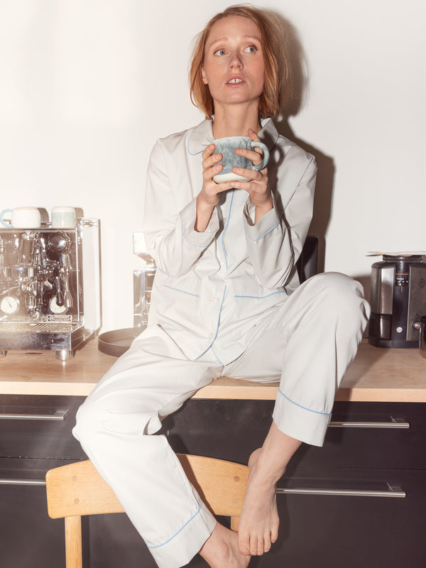Kvinde i hvid pyjamas med lyseblå piping, siddende med en kop