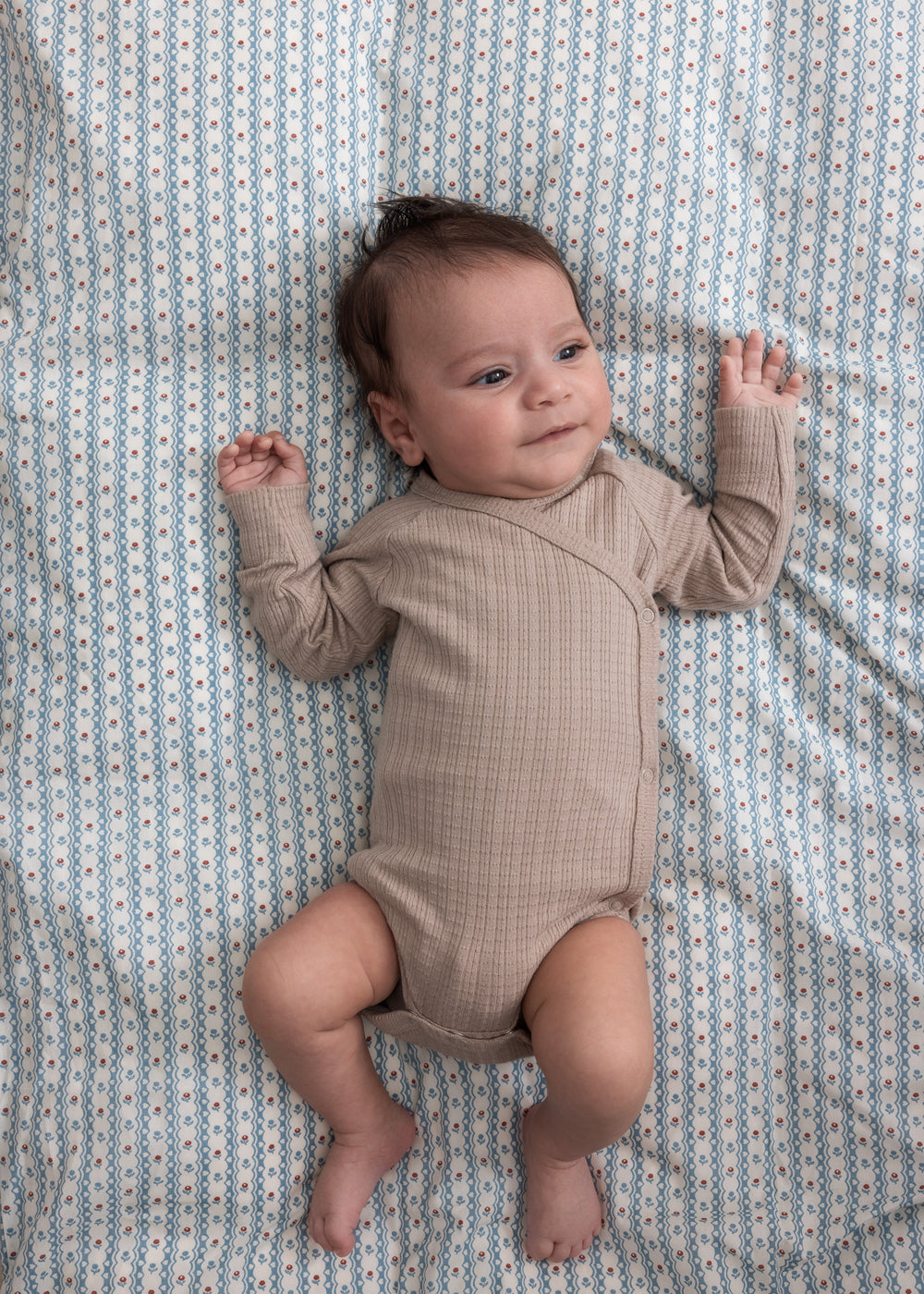 Børn iført beige pointelle slå-om body liggende på et blåt mønstret tæppe