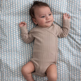 Børn iført beige pointelle slå-om body liggende på et blåt mønstret tæppe