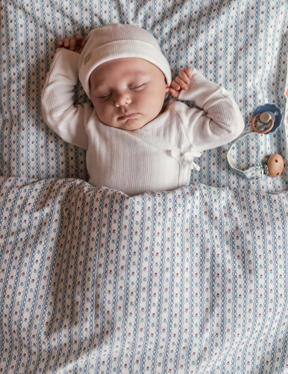 Baby wearing white pointelle hat lying on a blue patterned blanket