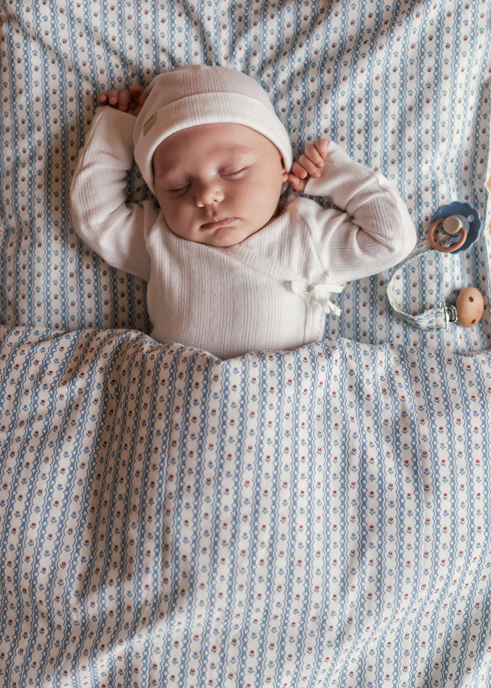 Baby iført hvid pointelle hue liggende på et blåt mønstret tæppe