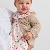 Baby iført beige cardigan med guldglimmer og lyserød julekjole med juleklokke mønster