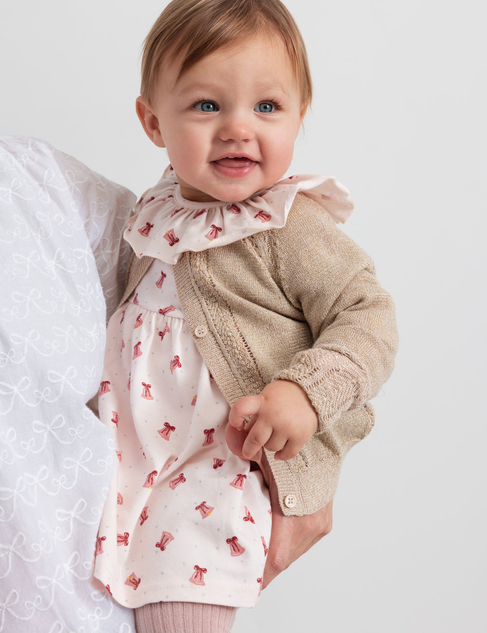 Baby wearing dress with red Christmas bells and cream cardigan