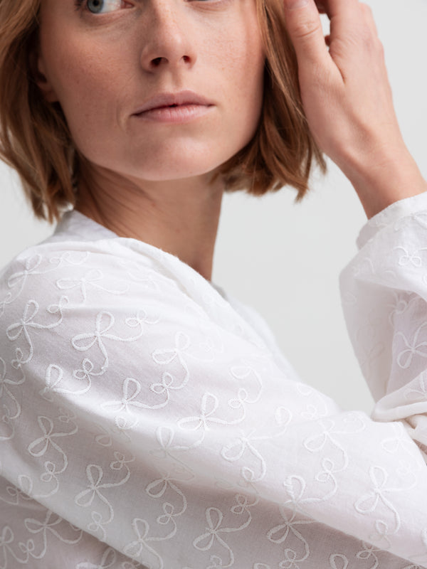 Kvinde i hvid bluse med broderede sløjfer