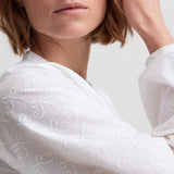 Kvinde iført hvid skjortebluse med broderet mønster