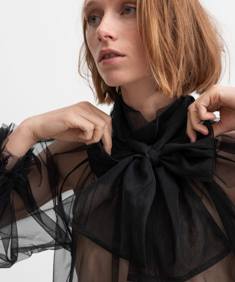 Kvinde iført sort gennemsigtig tylbluse med stor sløjfe
