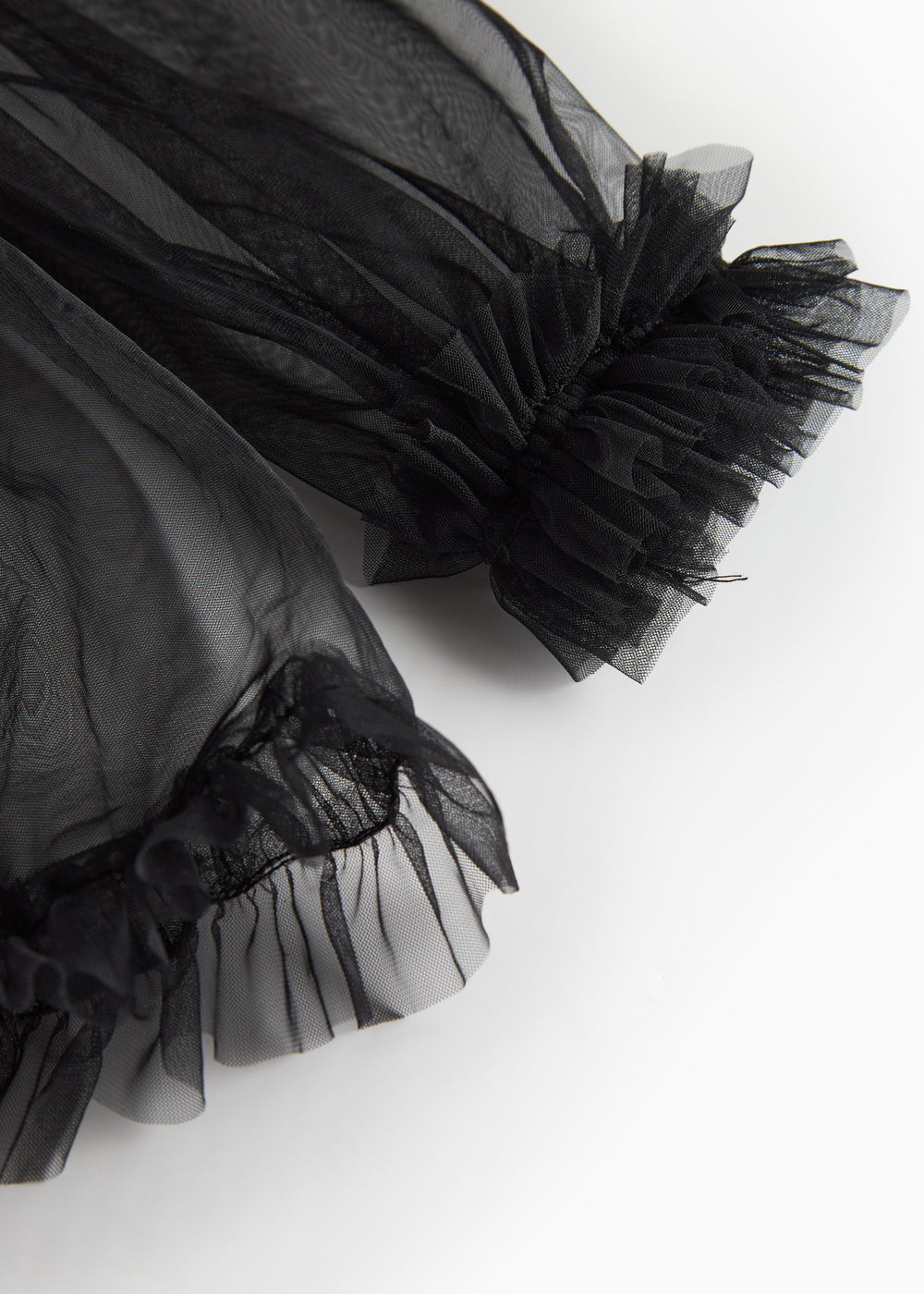 Detalje af sort tylbluse med flæser ved ærmekant