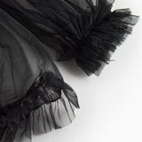 Detalje af sort tylbluse med flæser ved ærmekant