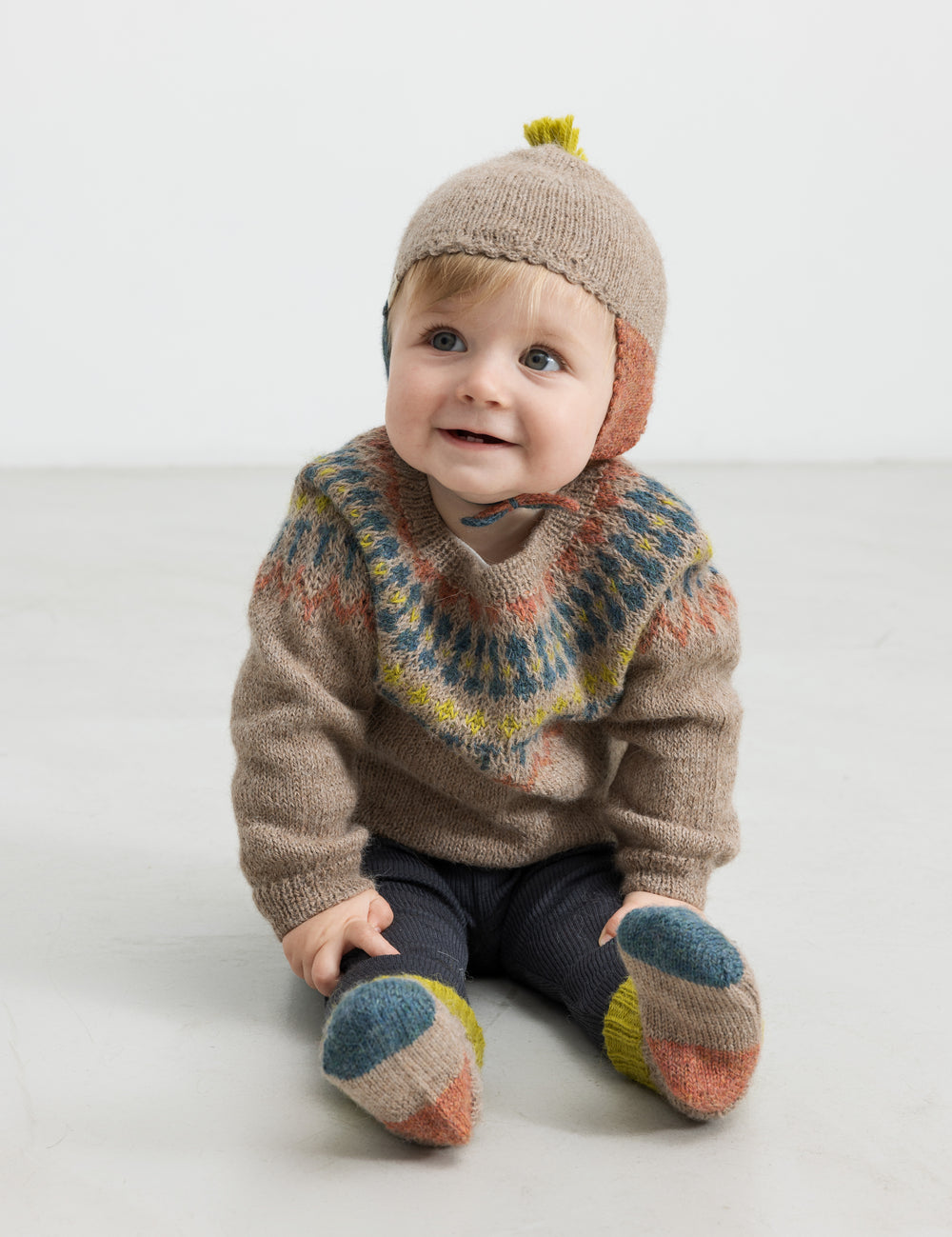 Baby med beige uldstrikbluse og mønster og uldhue