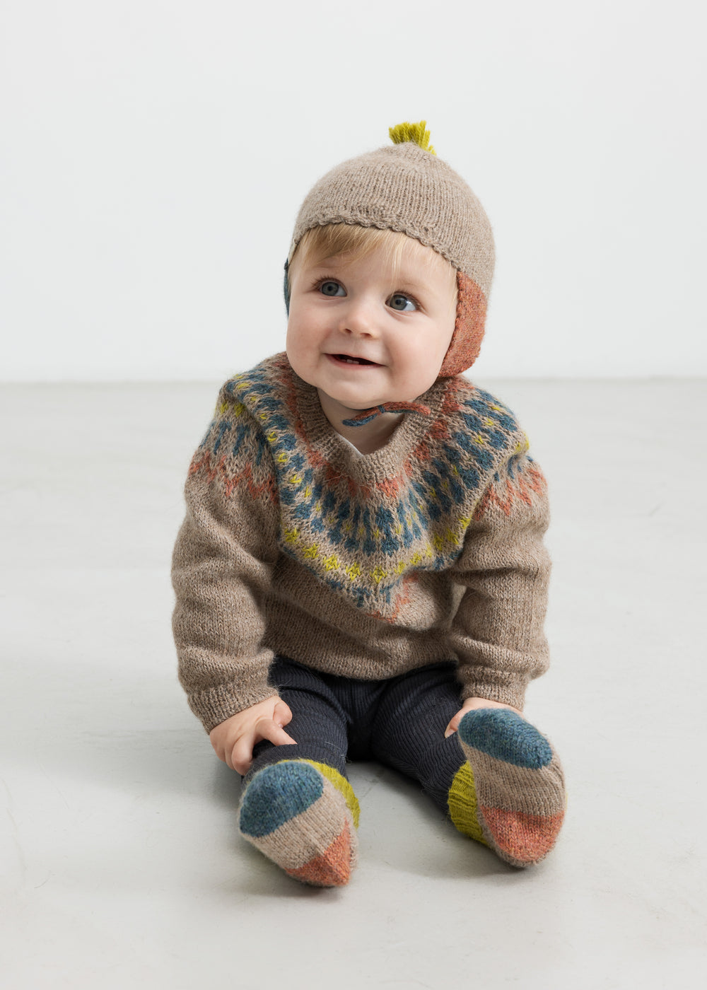 Baby iført beige uldstrikbluse med mønster og uldhue