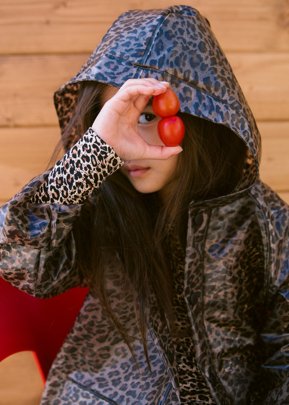 Barn iført leopardmønstret regnjakke me hætte, kigger gennem et tomatstykke